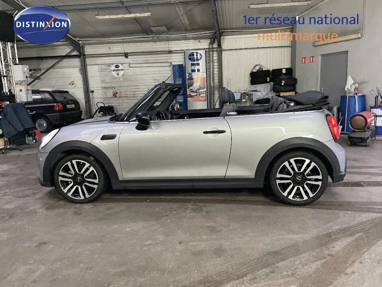 Profil droit d'une MINI Cabriolet 2023 couleur Melting Silver Metal avec capote ouverte dans un garage.