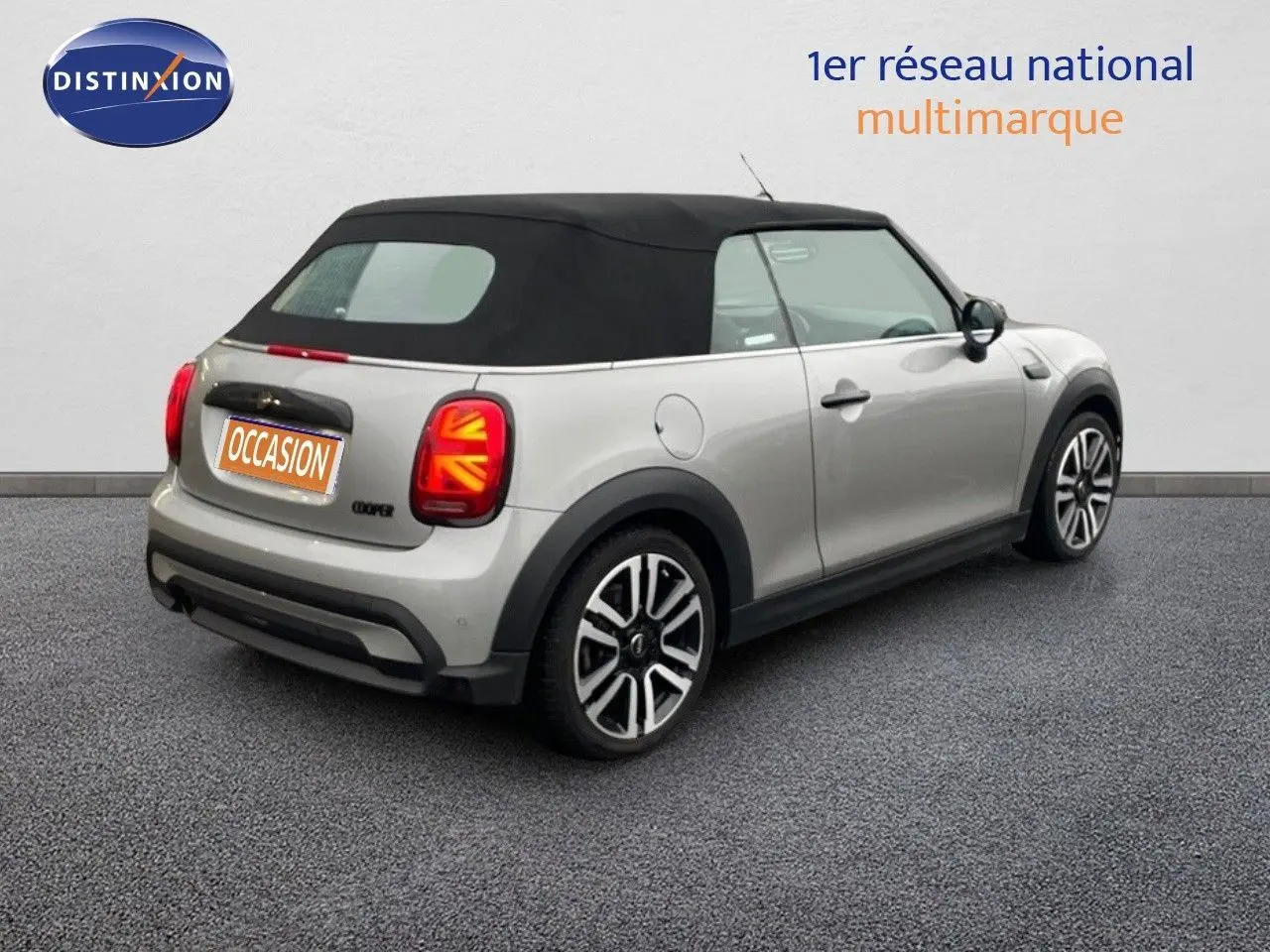 Vue 3/4 arrière droite d'une MINI Cabriolet 2023 Melting Silver avec toit noir et feux arrière à motif Union Jack.