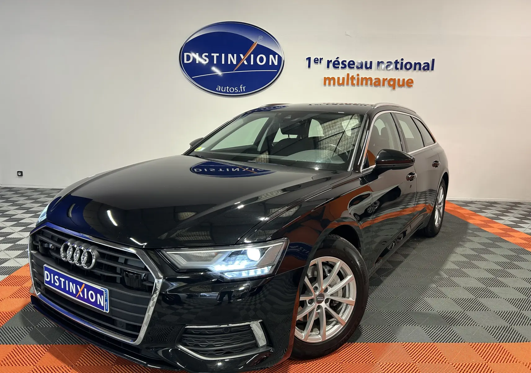 Audi A6 Avant noire vue en 3/4 avant droit avec phares allumés dans un showroom multimarque