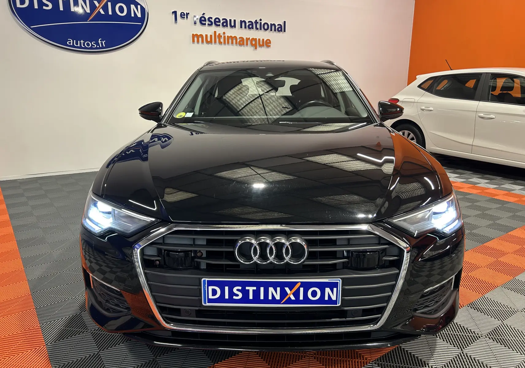 Audi A6 Avant noir vue de face avec phares allumés dans un showroom aux couleurs orange et gris.