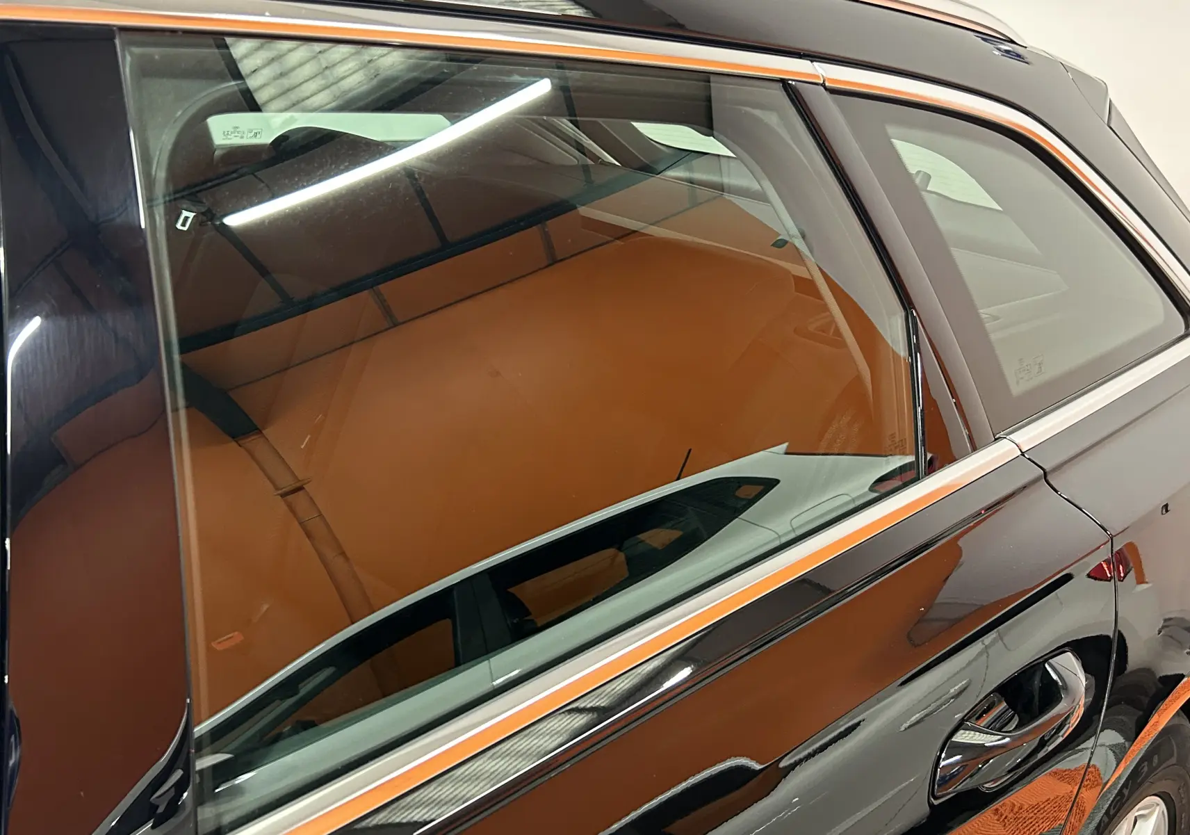 Gros plan sur la porte arrière droite noire d'une Audi A6 Avant 40 TDI 2019, reflet et intérieur cuir marron visibles.