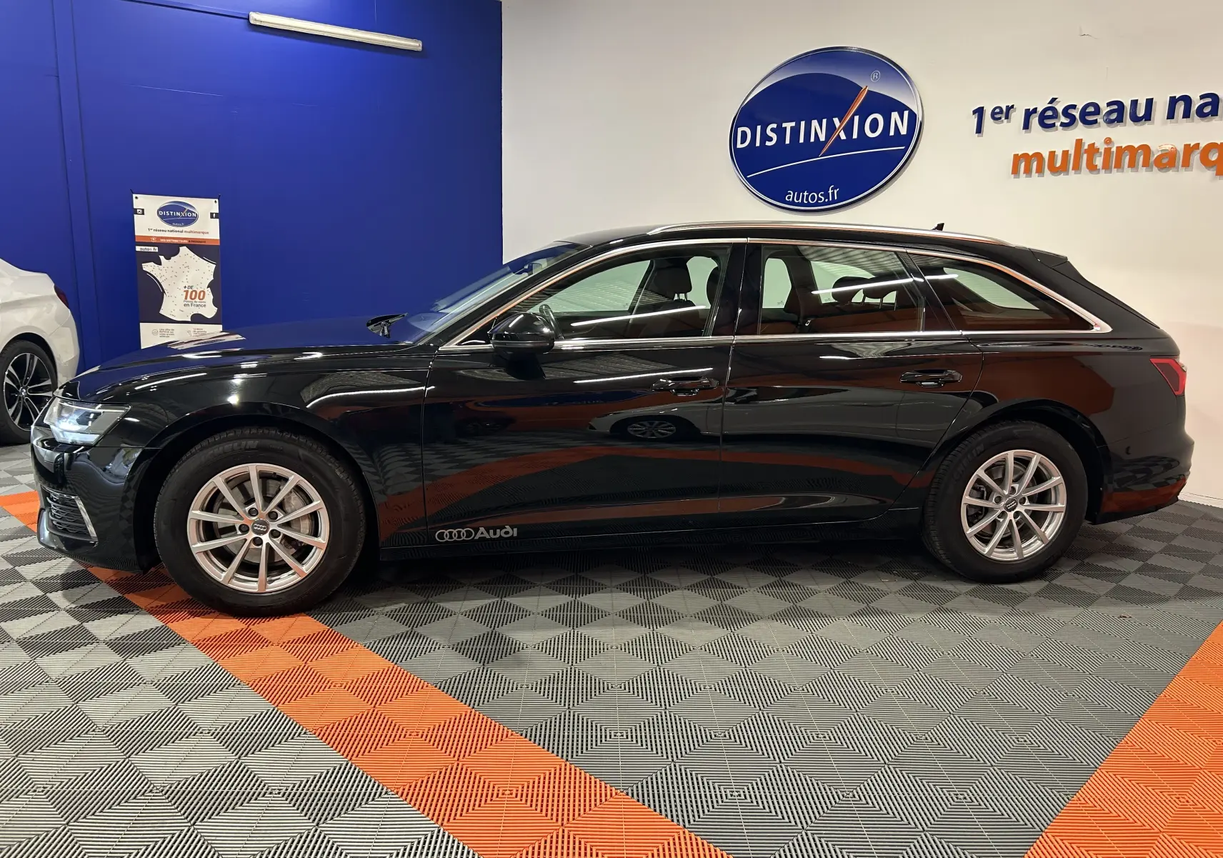 Profil côté gauche d'une Audi A6 Avant 40 TDI noire de 2019, en intérieur sur sol à damiers gris et orange.