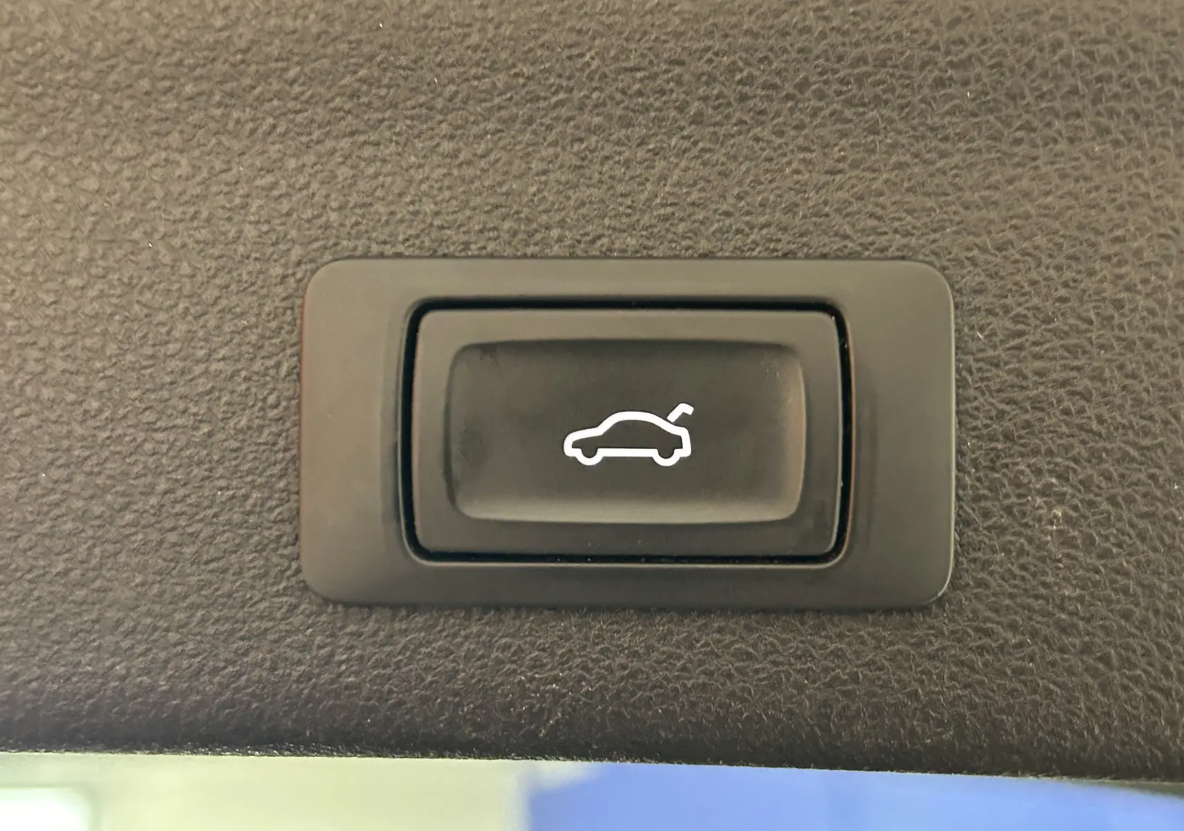 Bouton noir avec pictogramme blanc d'ouverture du coffre, situé à l'intérieur d'une Audi A6 Avant noire de 2019.