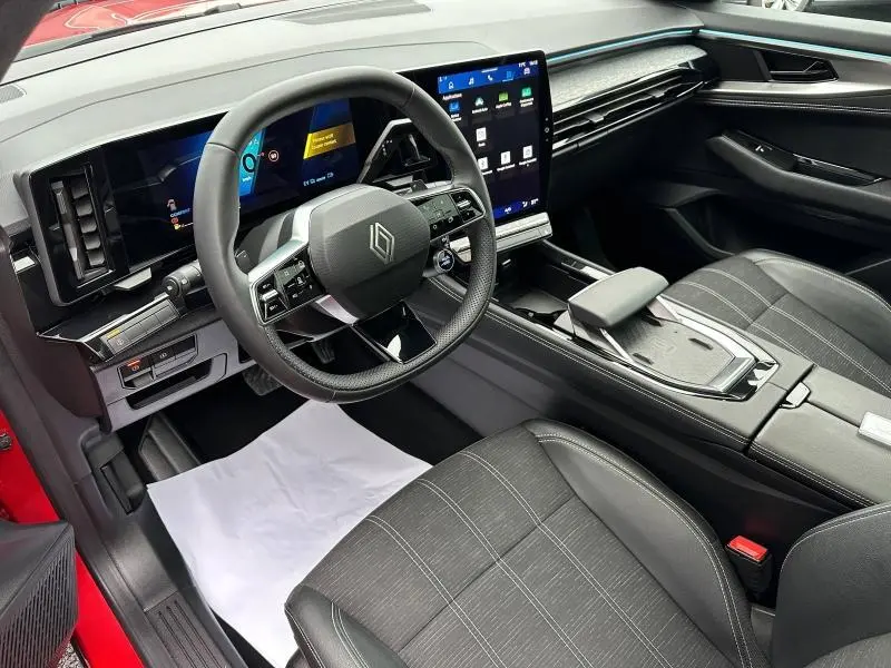 Vue intérieure côté conducteur du Renault Austral 2025 rouge flamme, avec tableau de bord numérique et écran tactile vertical.