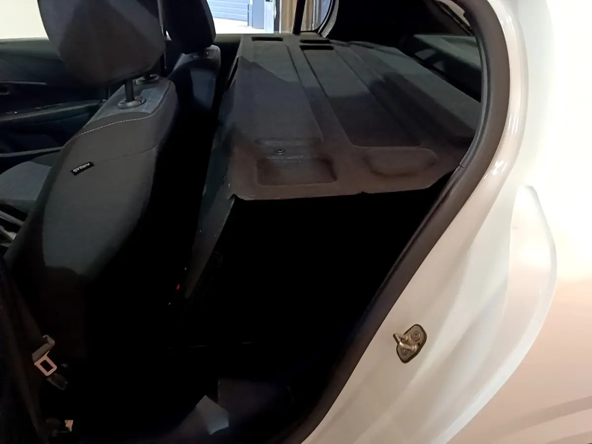 Vue intérieure côté gauche du coffre ouvert d'une Peugeot 208 blanche, montrant la banquette arrière rabattue.