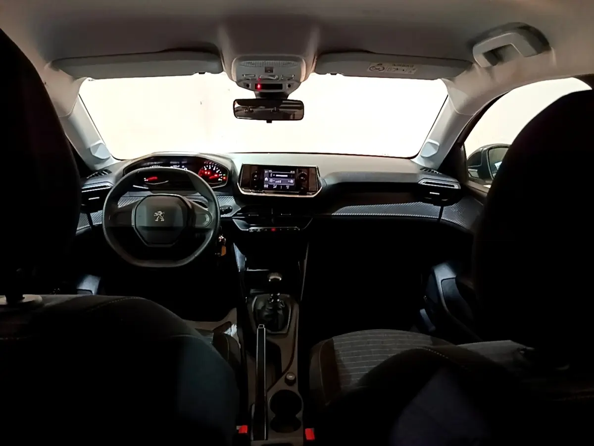 Vue intérieure avant de la Peugeot 208 blanche, tableau de bord moderne avec écran tactile et volant compact.