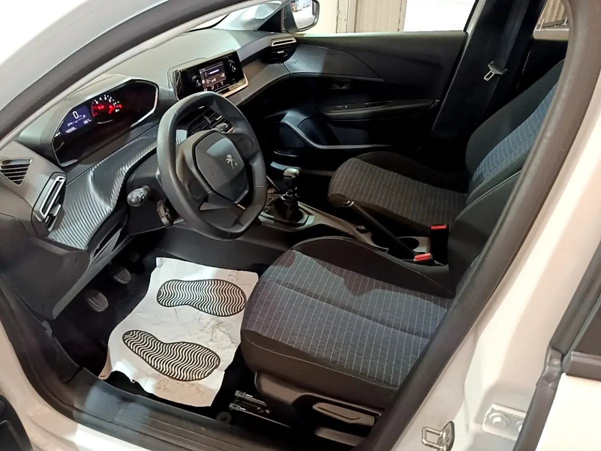 Vue intérieure côté conducteur de la Peugeot 208 blanche 2022, montrant le volant, tableau de bord digital et sièges tissu gris.