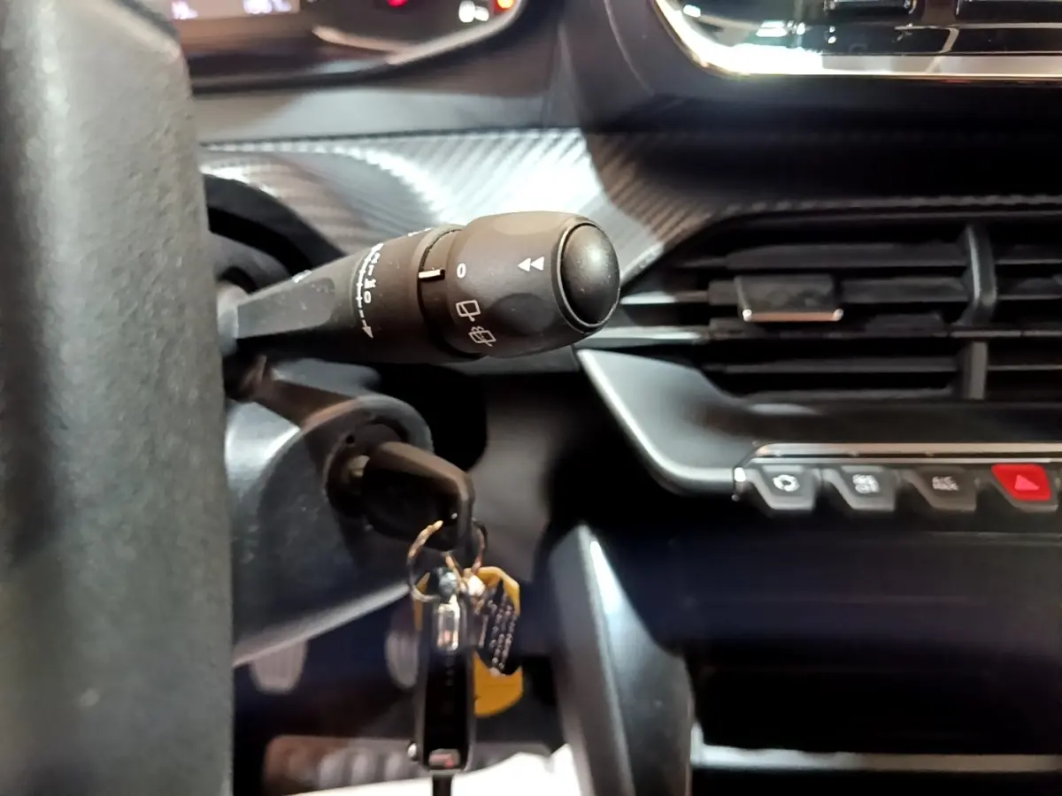 Gros plan sur la commande d’essuie-glace et la clé de contact insérée dans le tableau de bord noir de la Peugeot 208 blanche.