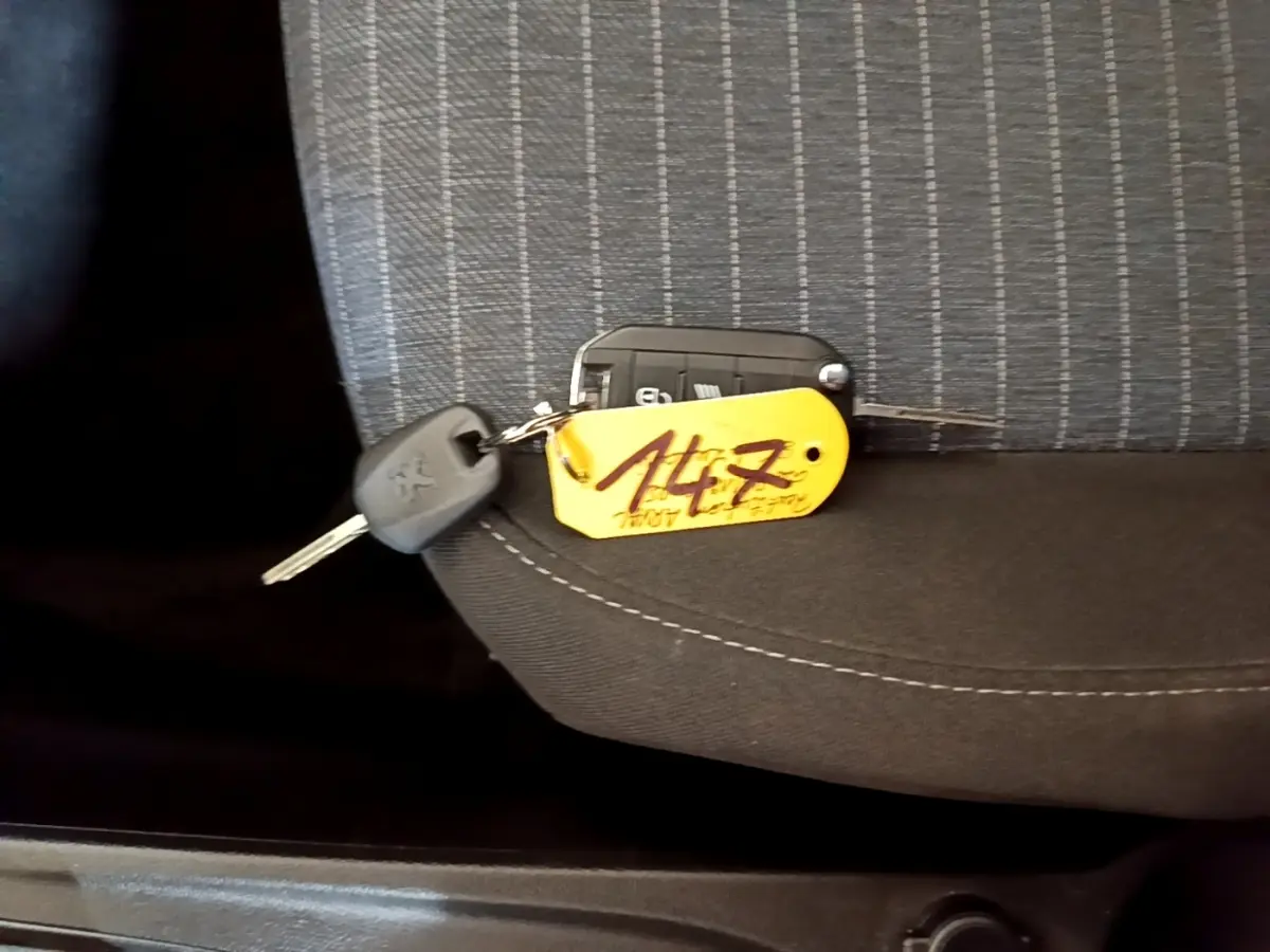 Clé de Peugeot 208 diesel 2022 posée sur un siège tissu gris à motifs, avec porte-clés jaune marqué "147".