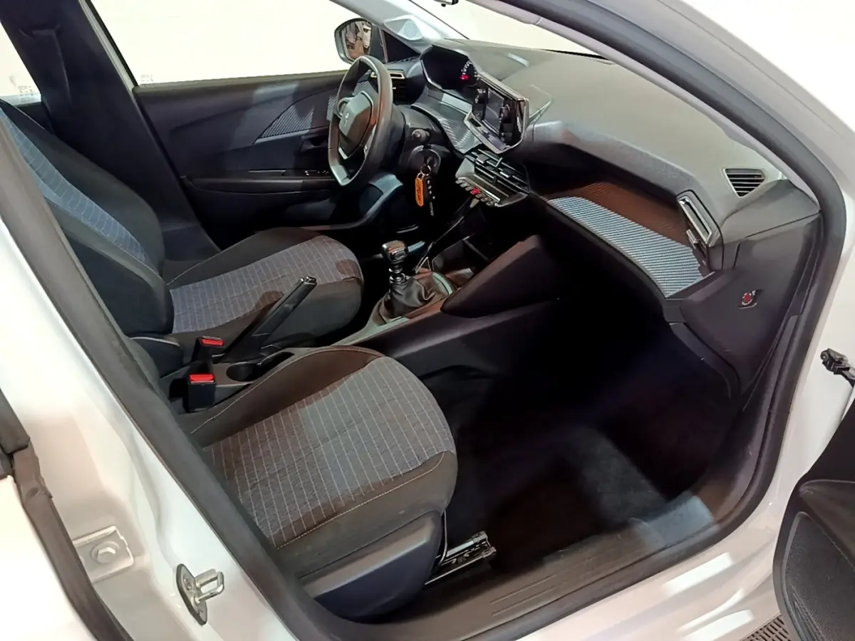 Intérieur avant droit d’une Peugeot 208 blanche 2022, montrant sièges tissu gris et tableau de bord avec écran tactile.