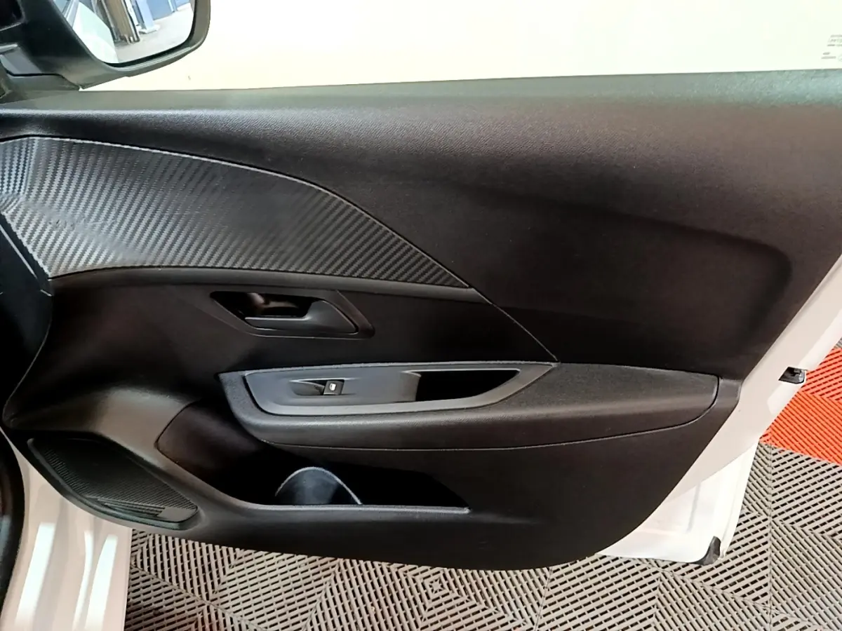 Vue rapprochée de la porte avant gauche blanche d’une Peugeot 208 2022 avec insert imitation carbone et commande de lève-vitre.