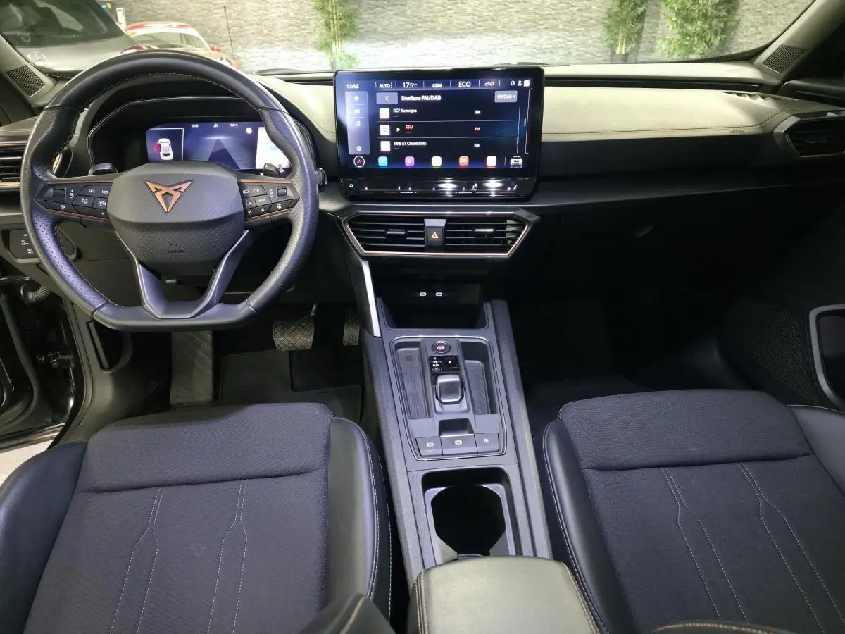 Vue intérieure avant du CUPRA Formentor 1.4 e-Hybrid 2023, tableau de bord noir avec écran tactile central et volant sport cuir.