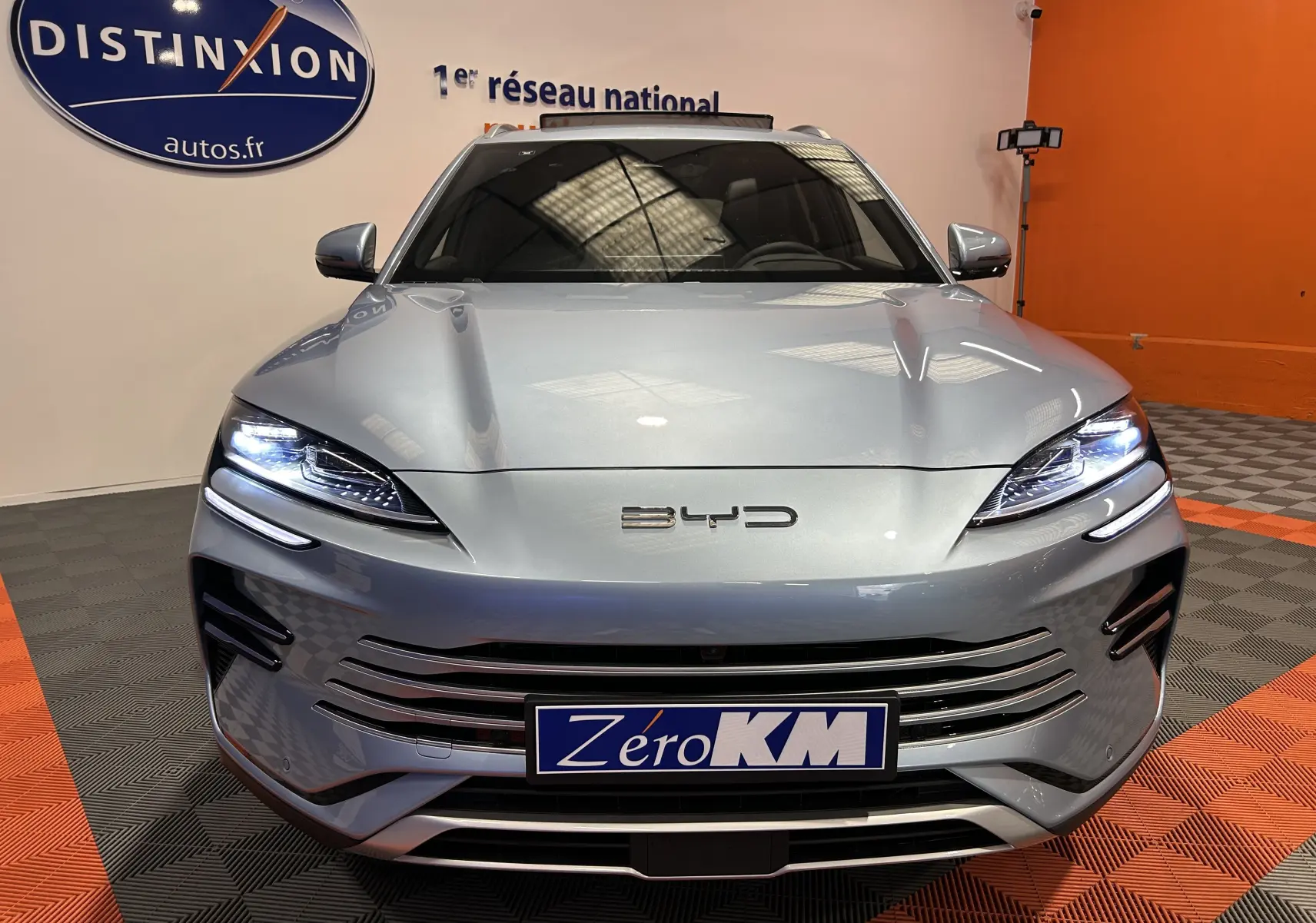 Vue frontale du BYD SEAL U hybride rechargeable en couleur Tian Qing Metal avec phares LED allumés dans un showroom.