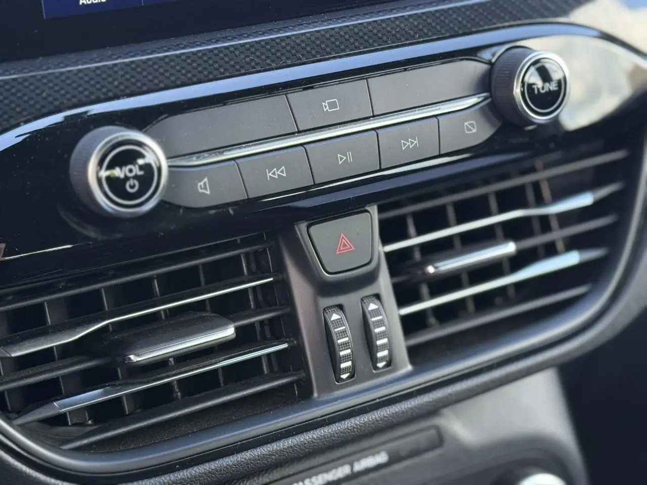 Gros plan sur la console centrale noire du Ford Kuga 2024, avec commandes audio et aérateurs horizontaux.