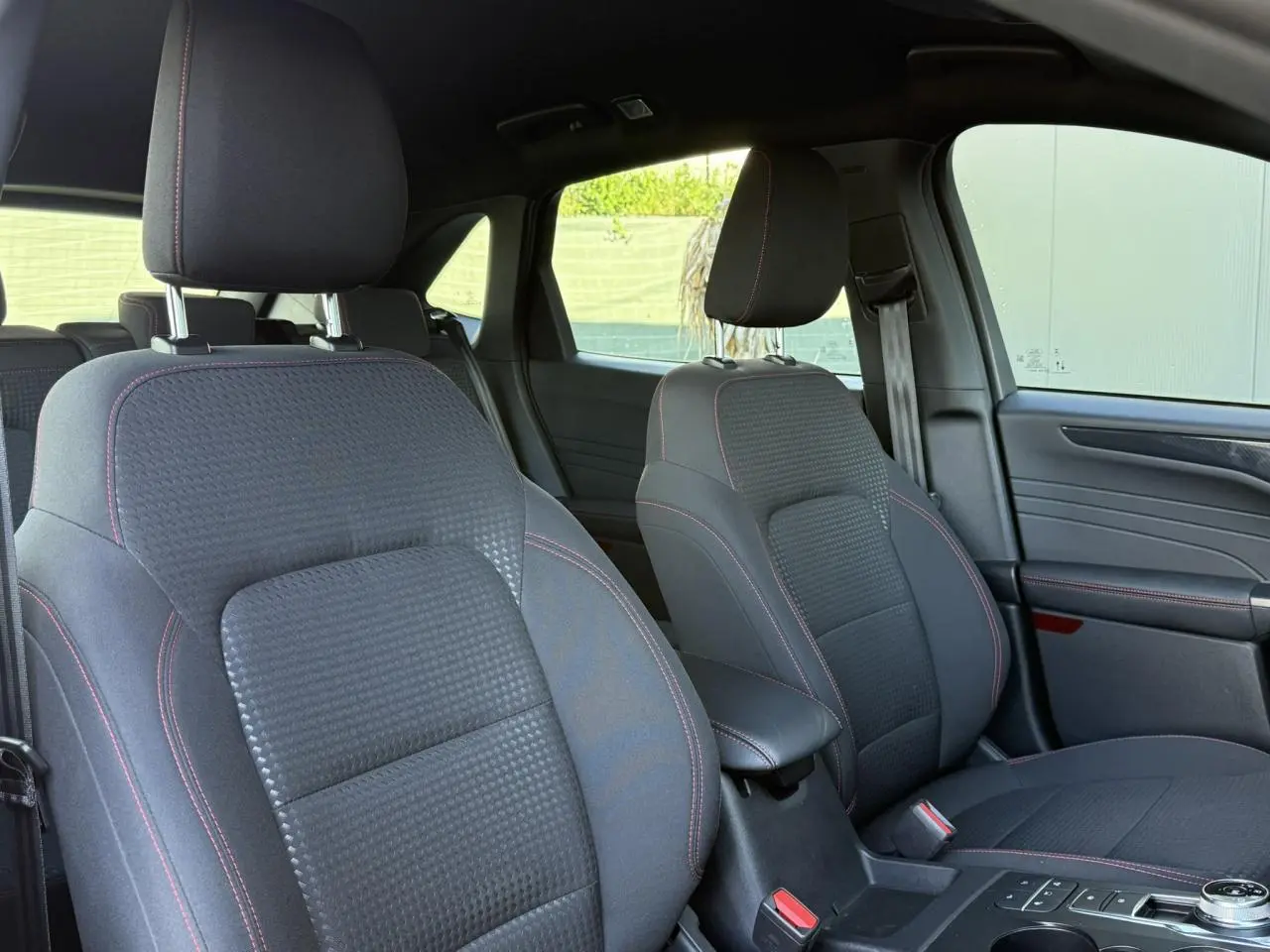 Vue intérieure avant du Ford Kuga 2024, sièges noirs avec surpiqûres rouges et console centrale avec sélecteur rotatif.