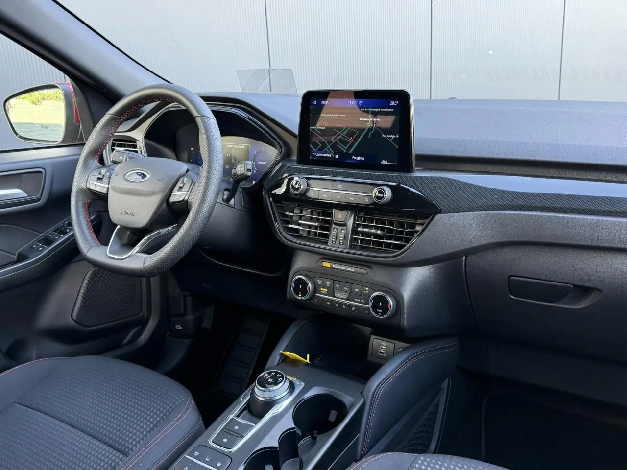 Vue intérieure côté conducteur du Ford Kuga 2024 avec volant ST-Line à surpiqûres rouges et écran tactile central.