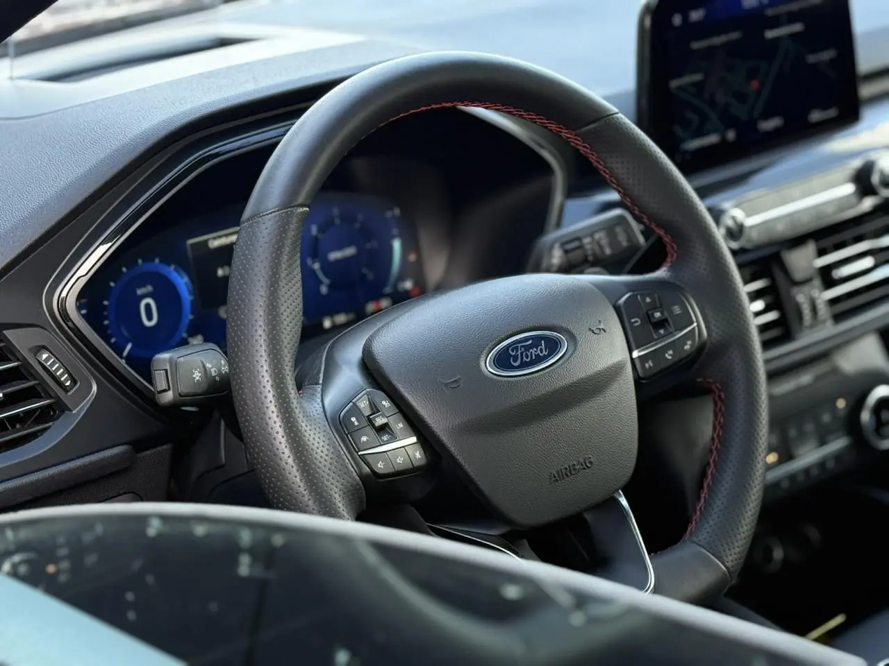 Vue rapprochée du volant noir avec surpiqûres rouges du Ford Kuga 2024 ST-Line, tableau de bord numérique en arrière-plan.