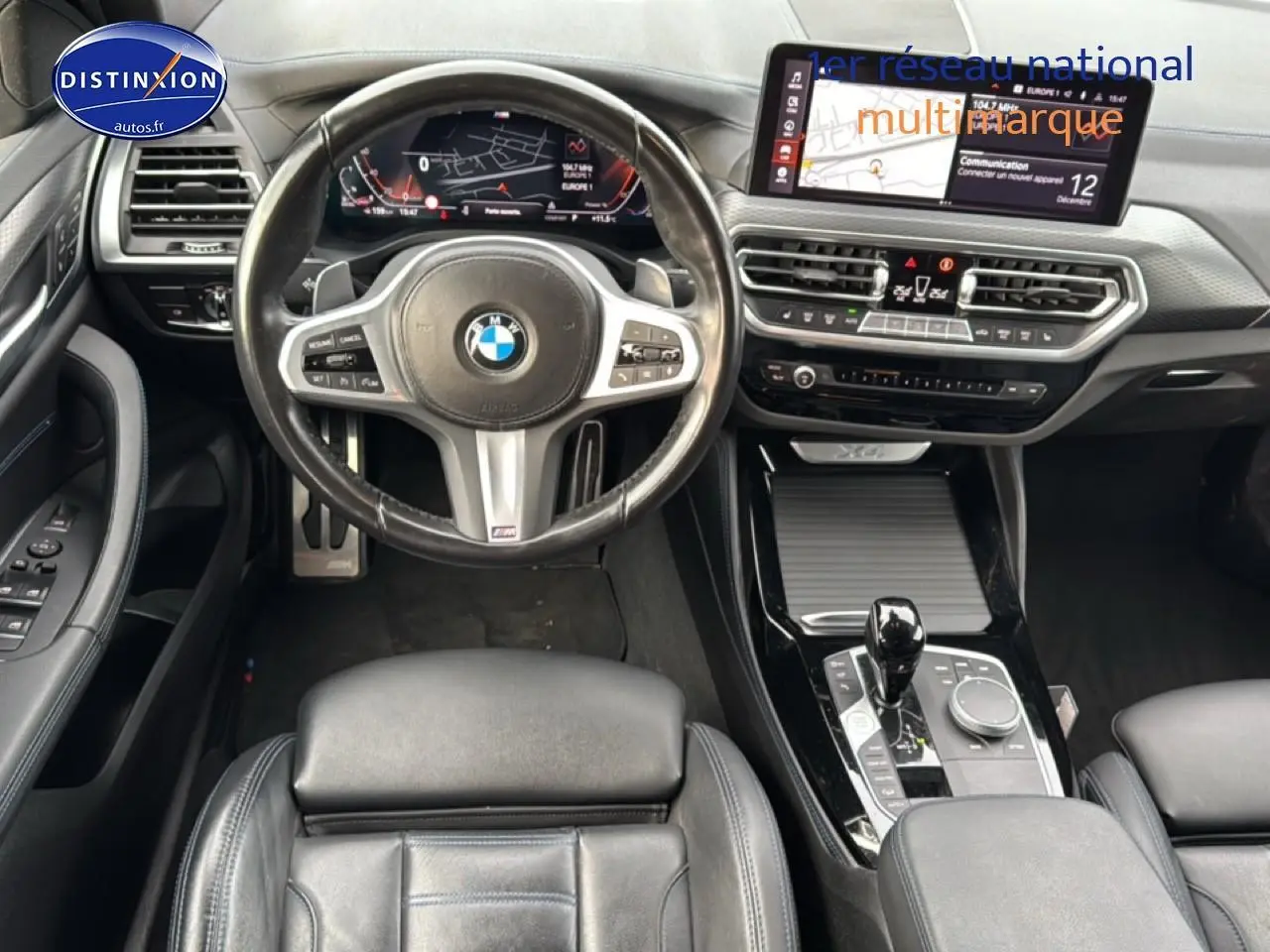 Vue intérieure centrée sur le volant cuir multifonction et la console centrale noire brillante d'une BMW X4 noire.