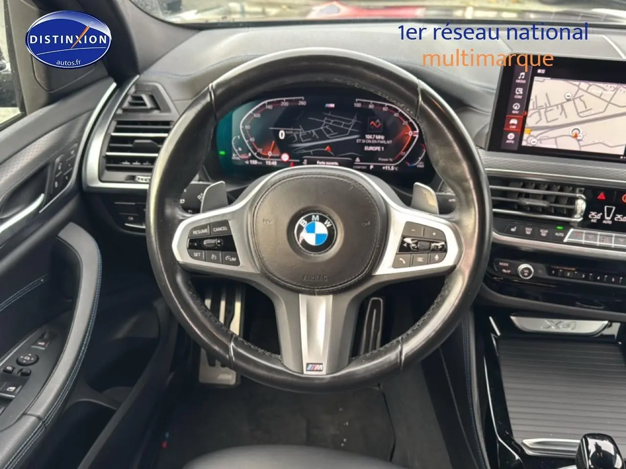 Vue intérieure centrée sur le volant cuir noir multifonction du BMW X4 (g02) xdrive30d 2022 avec tableau de bord digital et écran tactile.