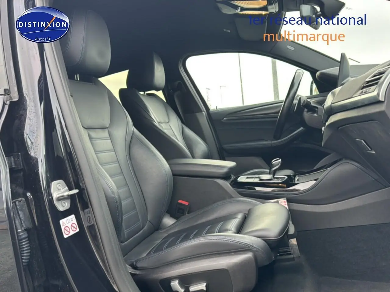 Intérieur avant côté conducteur d’une BMW X4 noire, sièges sport cuir noirs et console centrale avec accoudoir.
