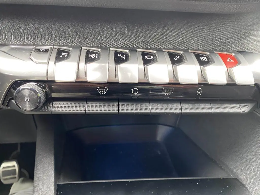 Gros plan sur la rangée de commandes centrales argentées et noires du tableau de bord du Peugeot 3008 blanc, version GT Line.