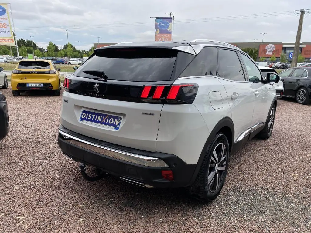 Peugeot 3008 blanc vue 3/4 arrière droit, feux arrière à triple griffes rouges et toit noir contrasté.