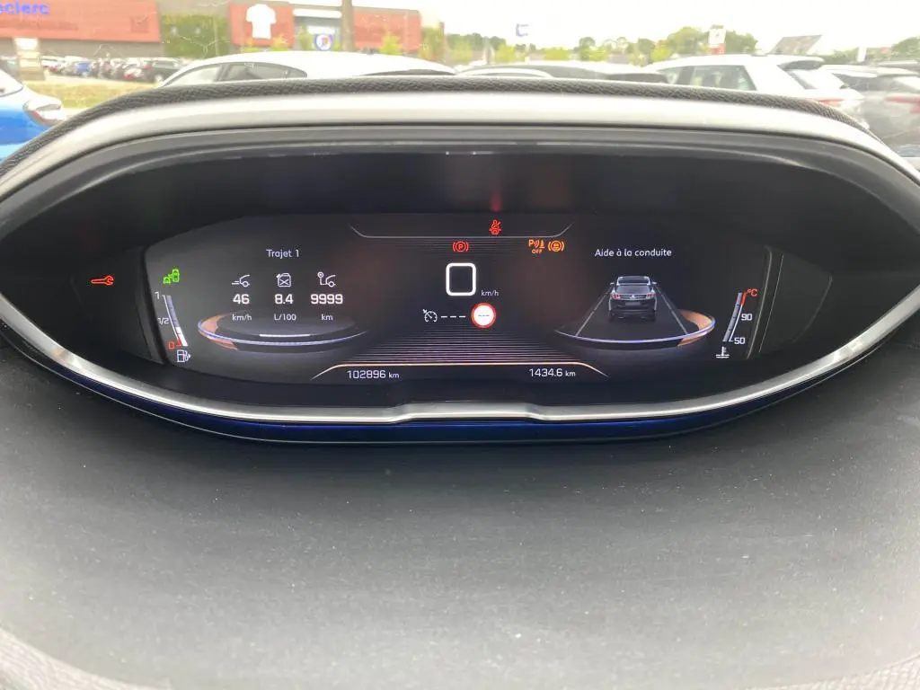 Affichage numérique du tableau de bord du Peugeot 3008 blanc, montrant la vitesse, consommation et aide à la conduite.