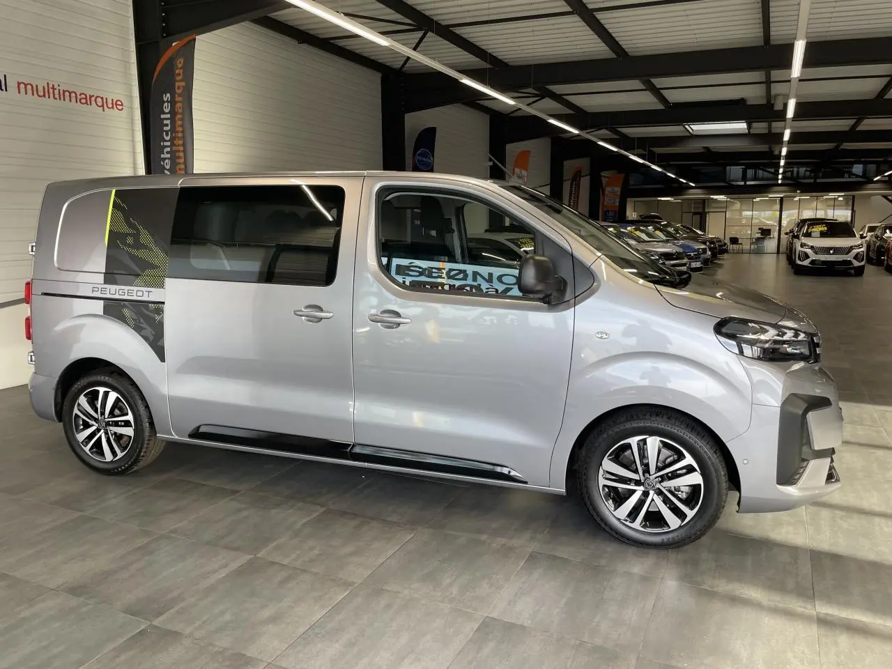Vue latérale droite du Peugeot Expert Fourgon gris Artense avec décor noir et jantes alliage 17 pouces en showroom.