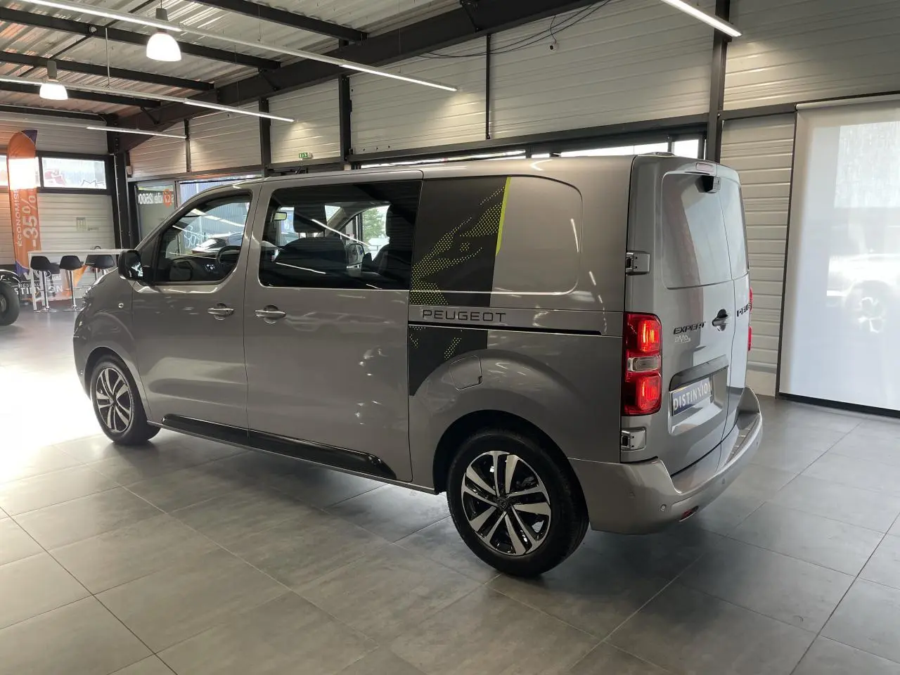 Vue 3/4 arrière droit du Peugeot Expert Fourgon gris Artense avec décor noir et vert sur la porte latérale.