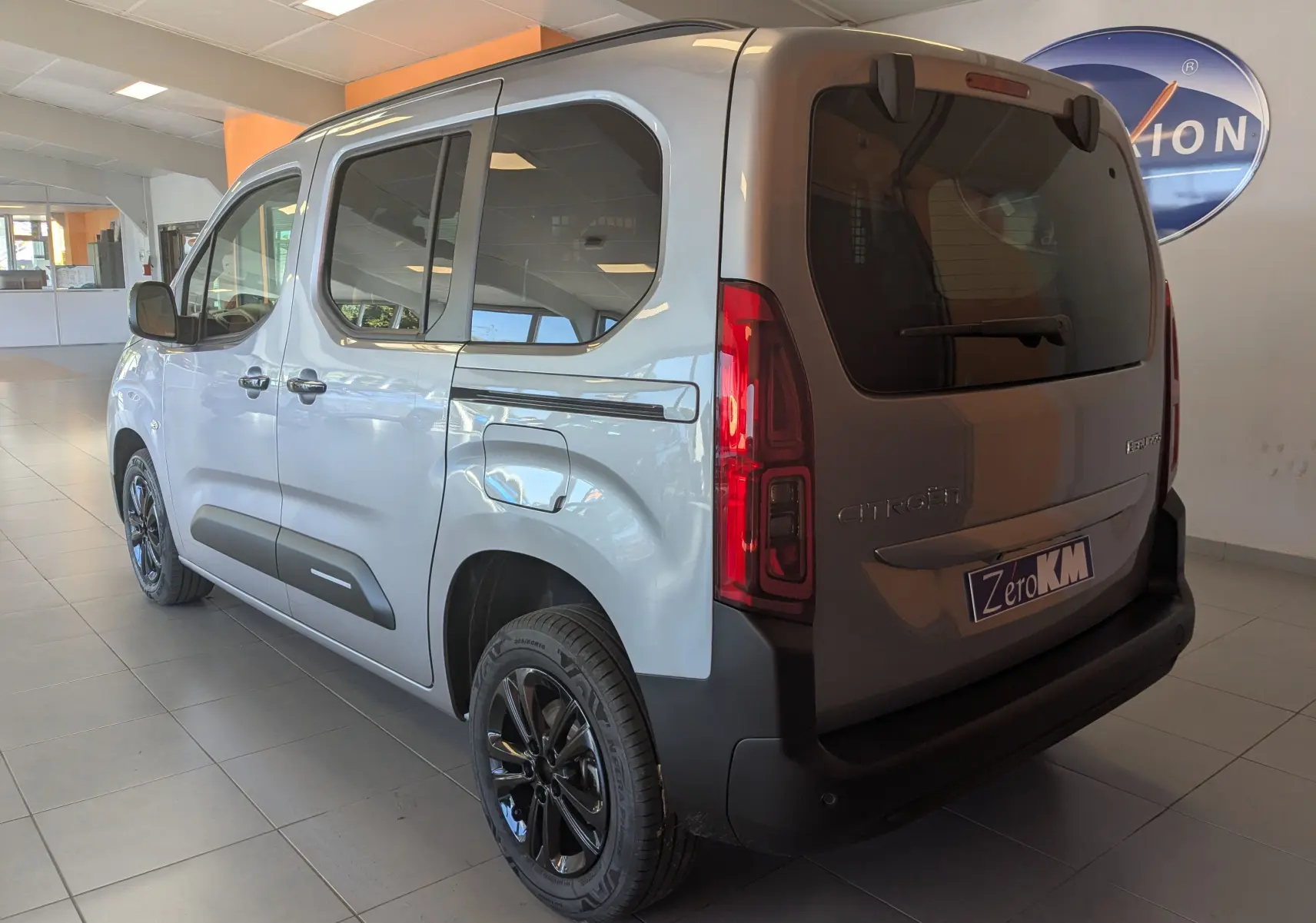 Vue 3/4 arrière droite du Citroën Berlingo gris Artense avec jantes noires et hayon fermé en intérieur showroom.