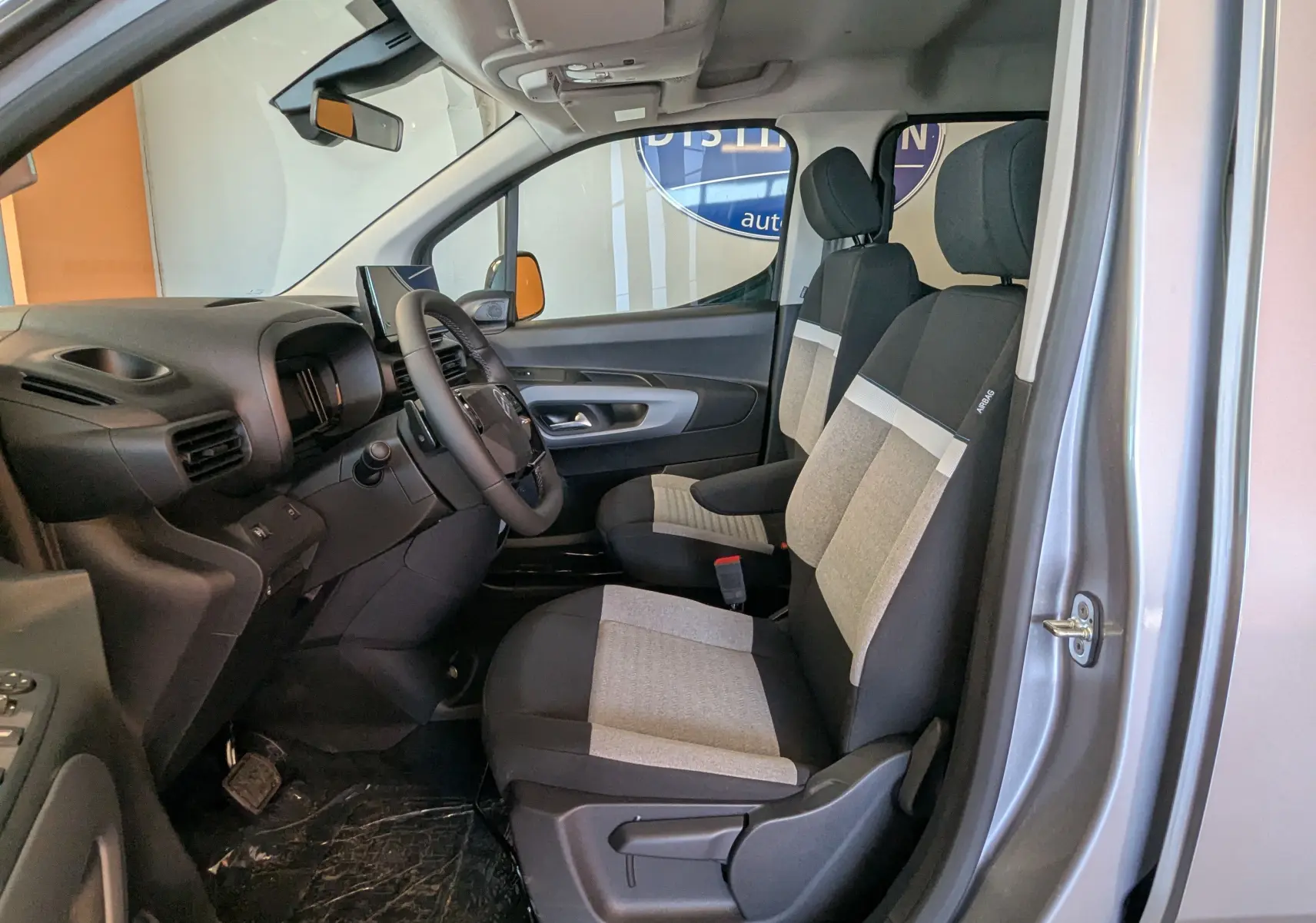 Vue intérieure côté conducteur du Citroën Berlingo gris Artense, montrant les sièges tissu bicolores et le tableau de bord moderne.