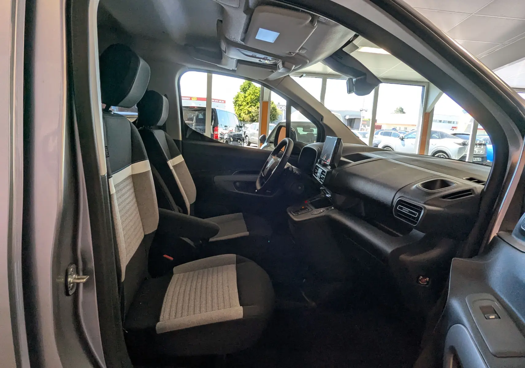 Vue intérieure côté conducteur du Citroën Berlingo gris Artense 2026, avec sièges tissu bicolore et tableau de bord moderne.