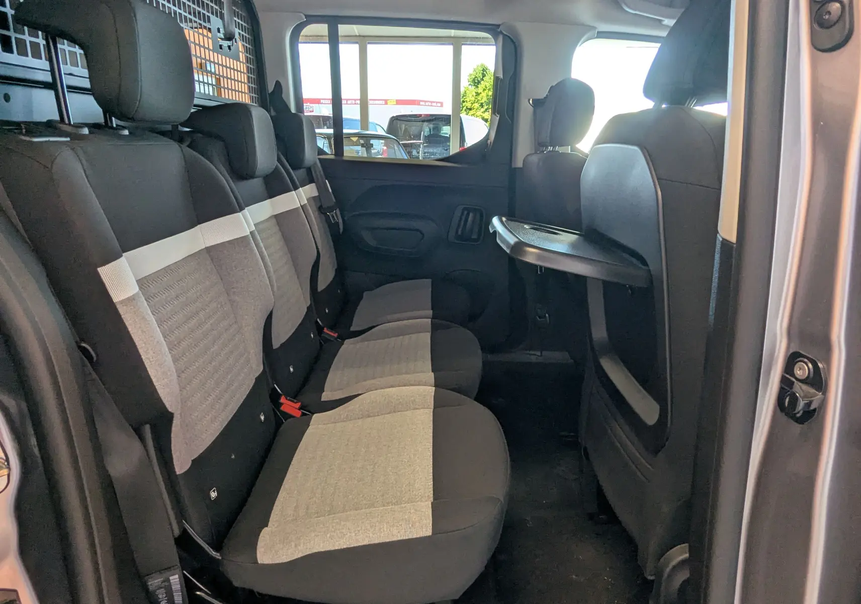 Vue intérieure côté droit des sièges arrière en tissu gris clair et noir du Citroën Berlingo gris Artense 2026 avec tablette rabattable.