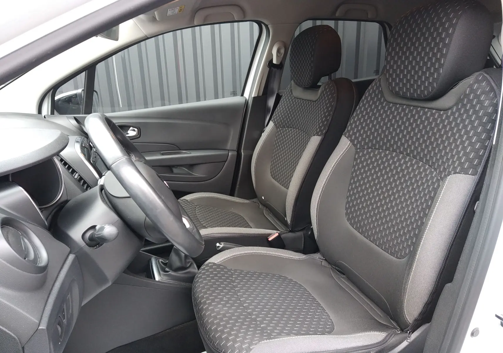 Vue intérieure côté conducteur du Renault Captur blanc 2017, mettant en valeur les sièges tissu gris et la boîte manuelle.
