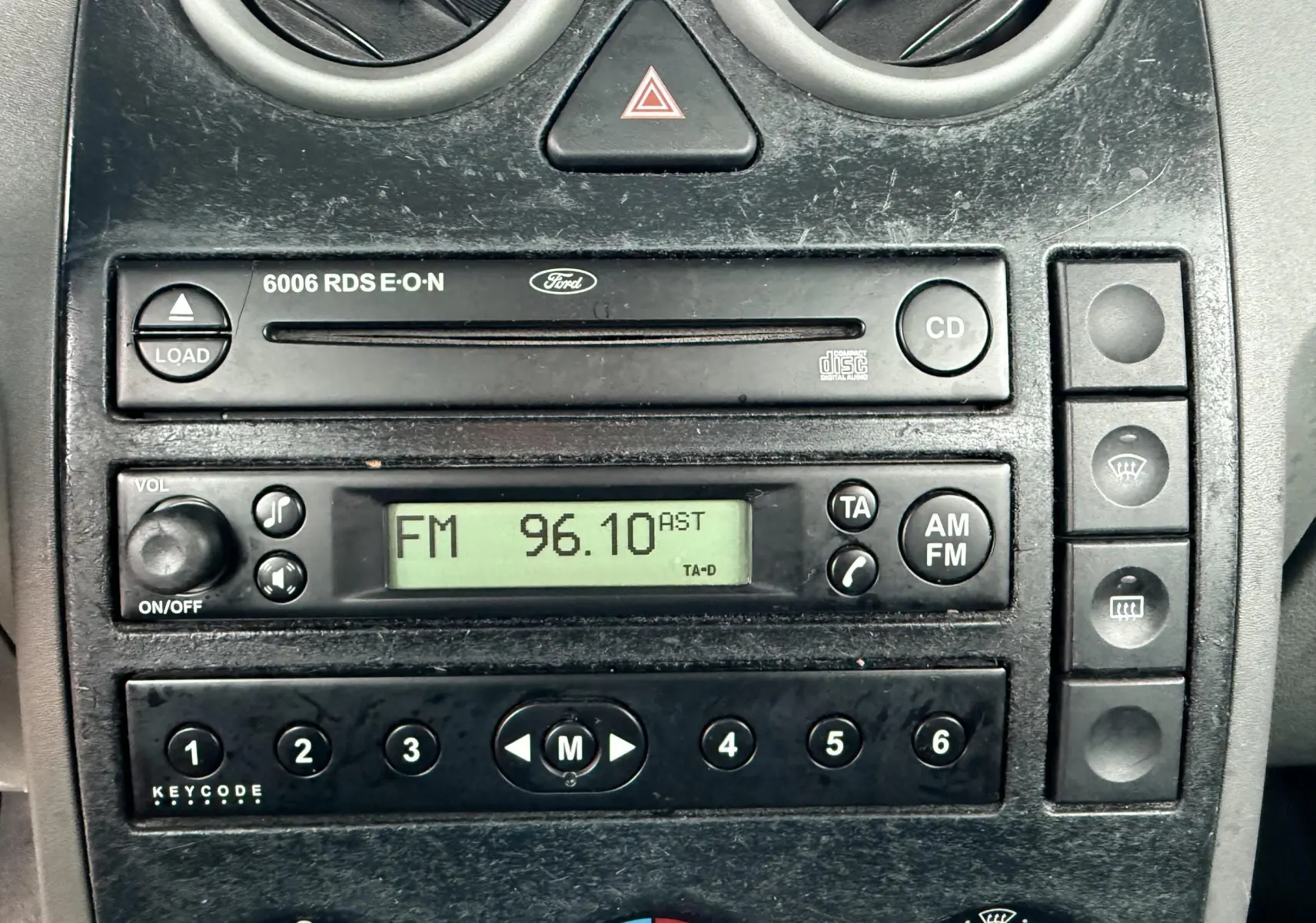 Gros plan sur la console centrale d'une Ford Fusion 2002, montrant l'autoradio CD et les commandes de climatisation.