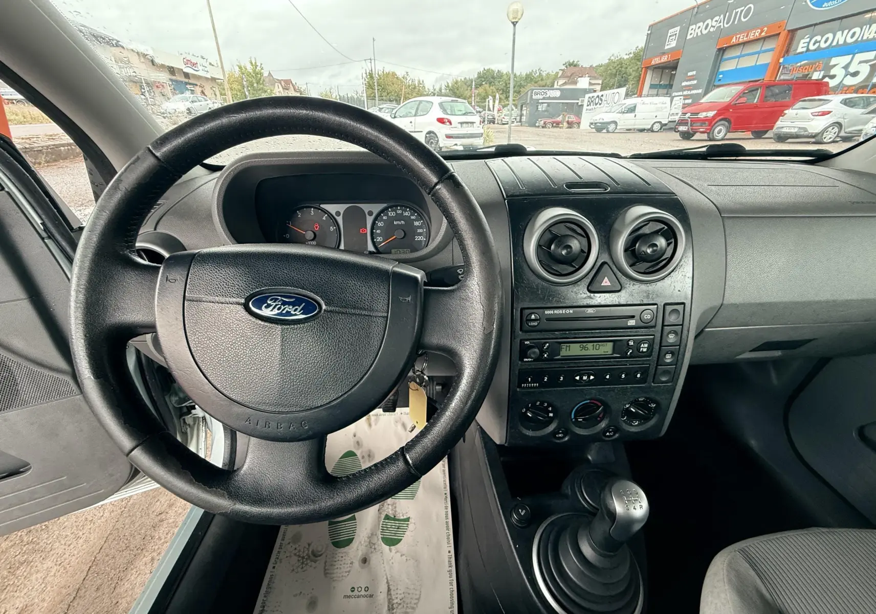 Vue intérieure centrée sur le volant Ford et la console centrale d'une Ford Fusion bleu clair de 2002 avec boîte manuelle.