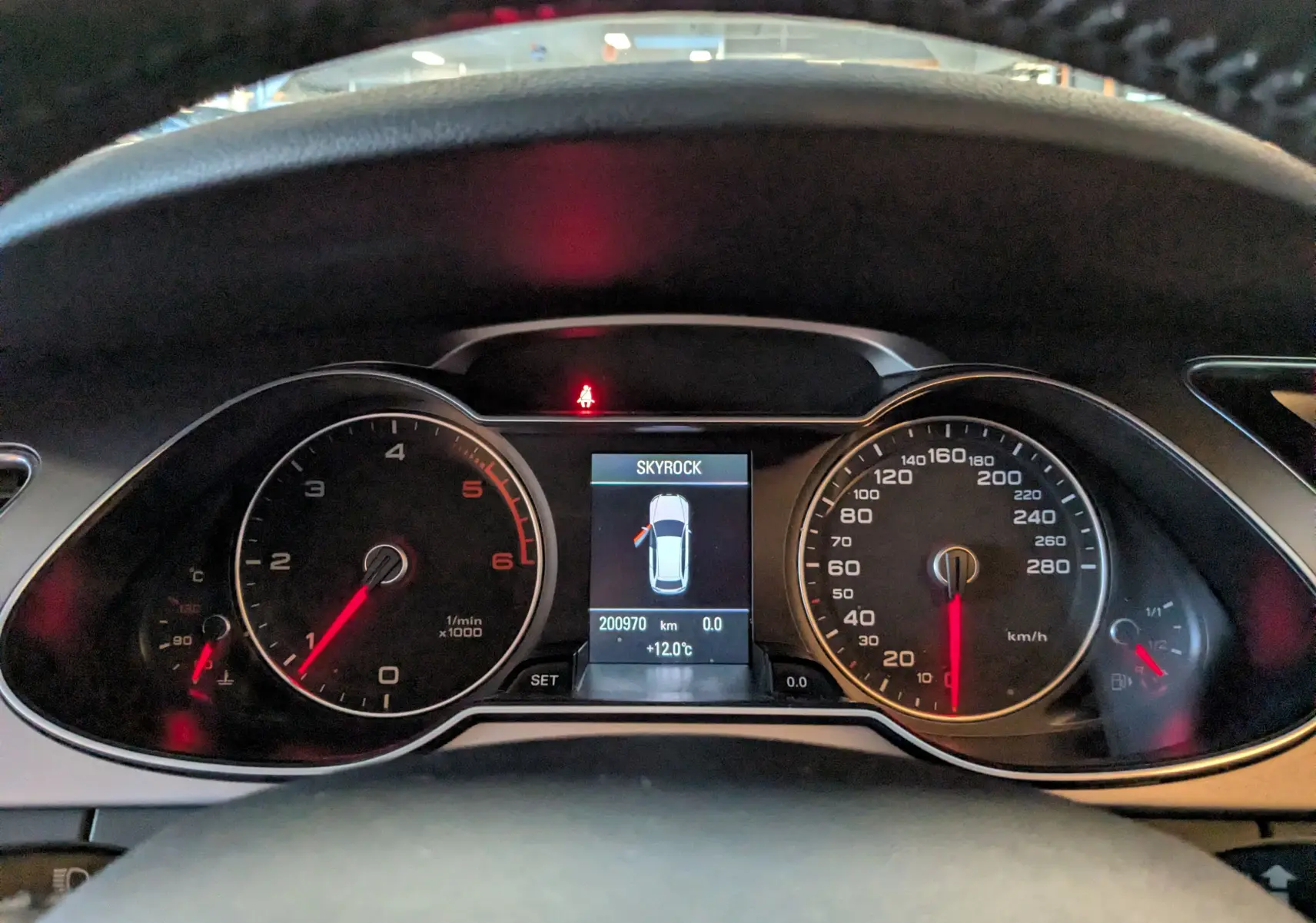 Tableau de bord de l'Audi A4 gris 2013 montrant compte-tours, vitesse et écran central avec porte ouverte à gauche.