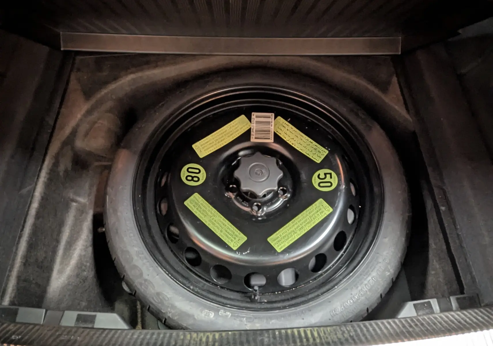 Vue en plongée sur la roue de secours noire avec étiquettes jaunes dans le coffre d'une Audi A4 gris diesel 2013