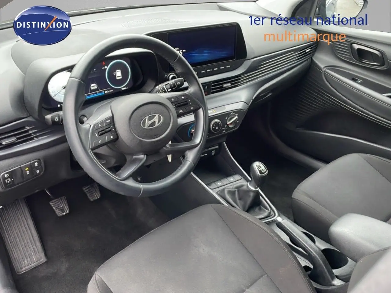 Vue intérieure côté conducteur de la Hyundai i20 2025 avec volant cuir, tableau de bord numérique et levier de vitesse manuel.