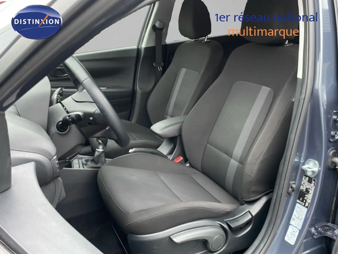 Vue intérieure côté conducteur de la Hyundai i20 gris Aurora Metal, montrant les sièges en tissu et cuir et le volant multifonction.