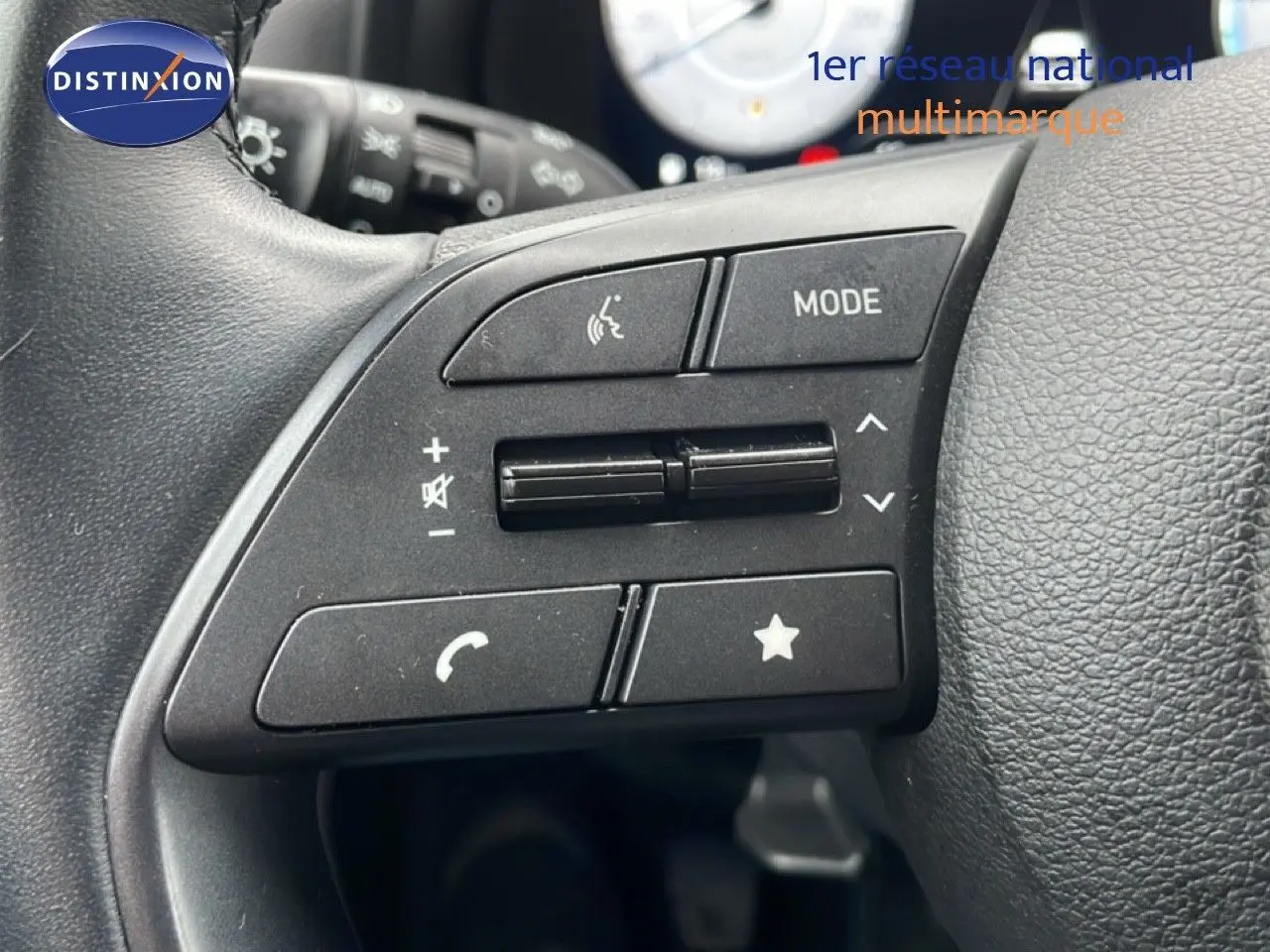 Gros plan sur les commandes gauche du volant noir de la Hyundai i20 2025, boutons mode, volume et téléphone visibles.