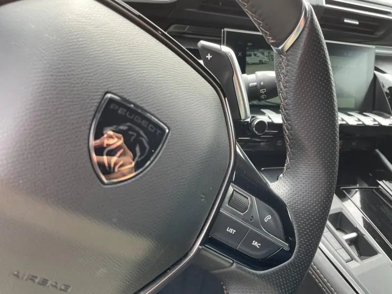 Gros plan sur le volant cuir perforé et les commandes multifonctions du Peugeot 508 SW gris Selenium, tableau de bord en arrière-plan.