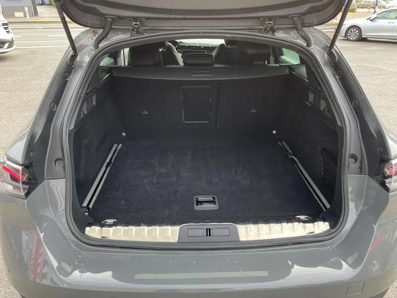 Coffre ouvert vu de l'arrière d'une Peugeot 508 SW 2024 gris Selenium, avec intérieur noir et seuil de chargement métallique.