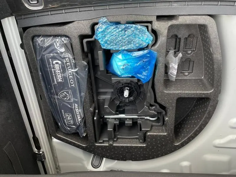 Vue plongeante sur le coffre ouvert d'une Peugeot 508 SW gris Selenium, montrant le rangement avec kit de secours emballé.