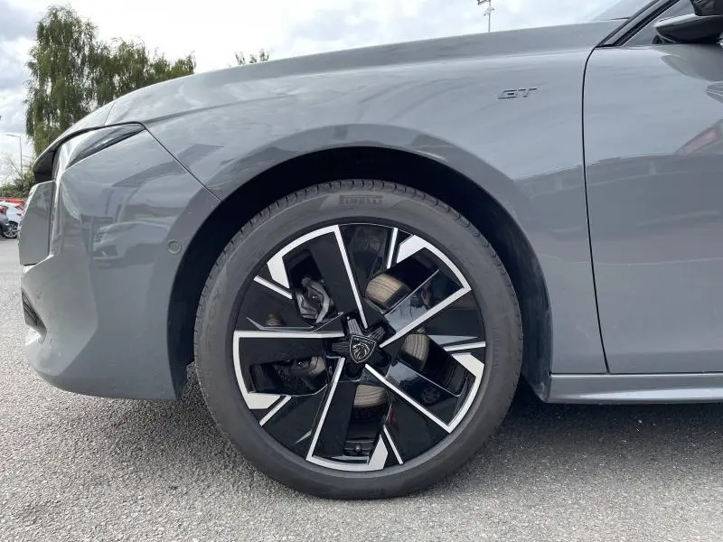 Gros plan sur la roue avant gauche et la partie latérale gris Selenium d'une Peugeot 508 SW GT 2024 avec jante alu noire et argent.