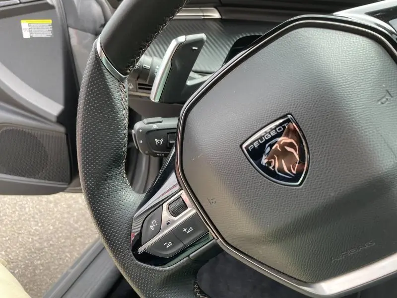Gros plan sur le volant cuir noir du Peugeot 508 SW 2024, avec commandes multifonctions et logo lion central.