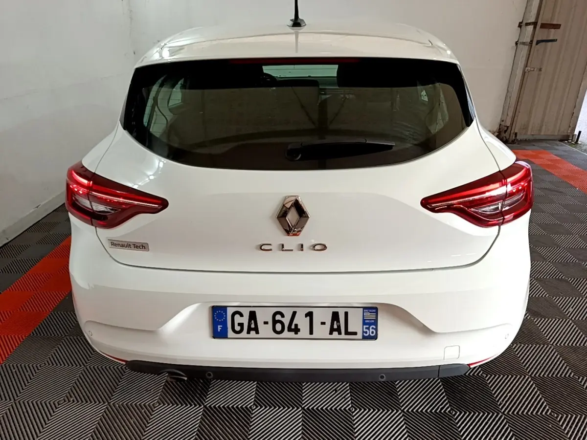 Vue arrière d'une Renault Clio blanche, avec feux arrière LED allumés et plaque d'immatriculation française visible.