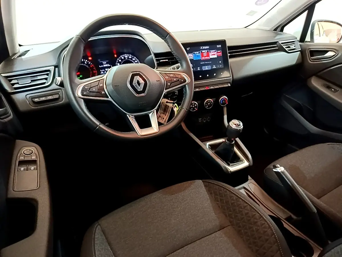 Vue intérieure avant droite de la Renault Clio Business blanche, volant cuir, écran tactile et boîte manuelle visible.