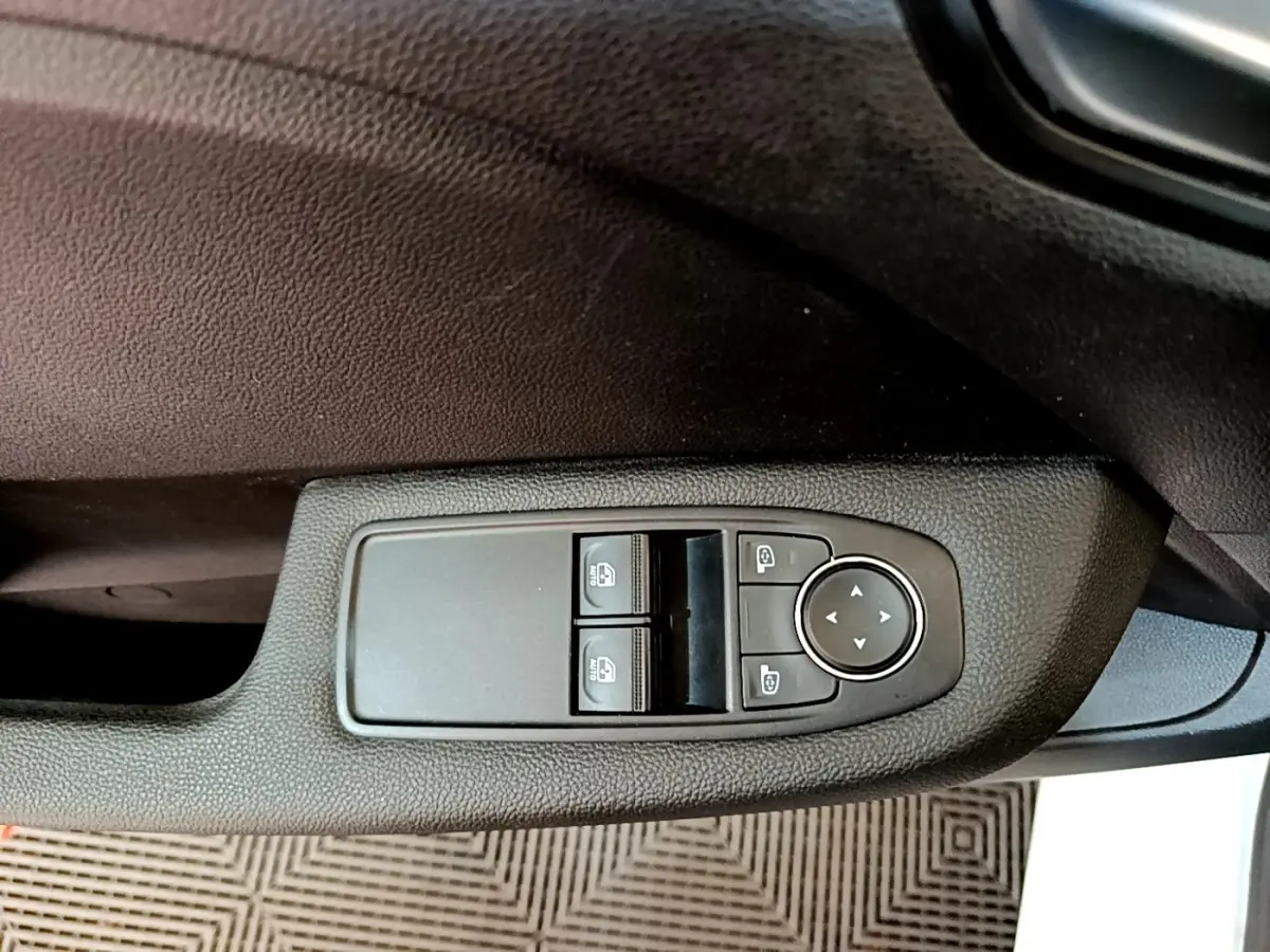 Détail des commandes de lève-vitres et rétroviseurs sur la porte côté conducteur d'une Renault Clio blanche.