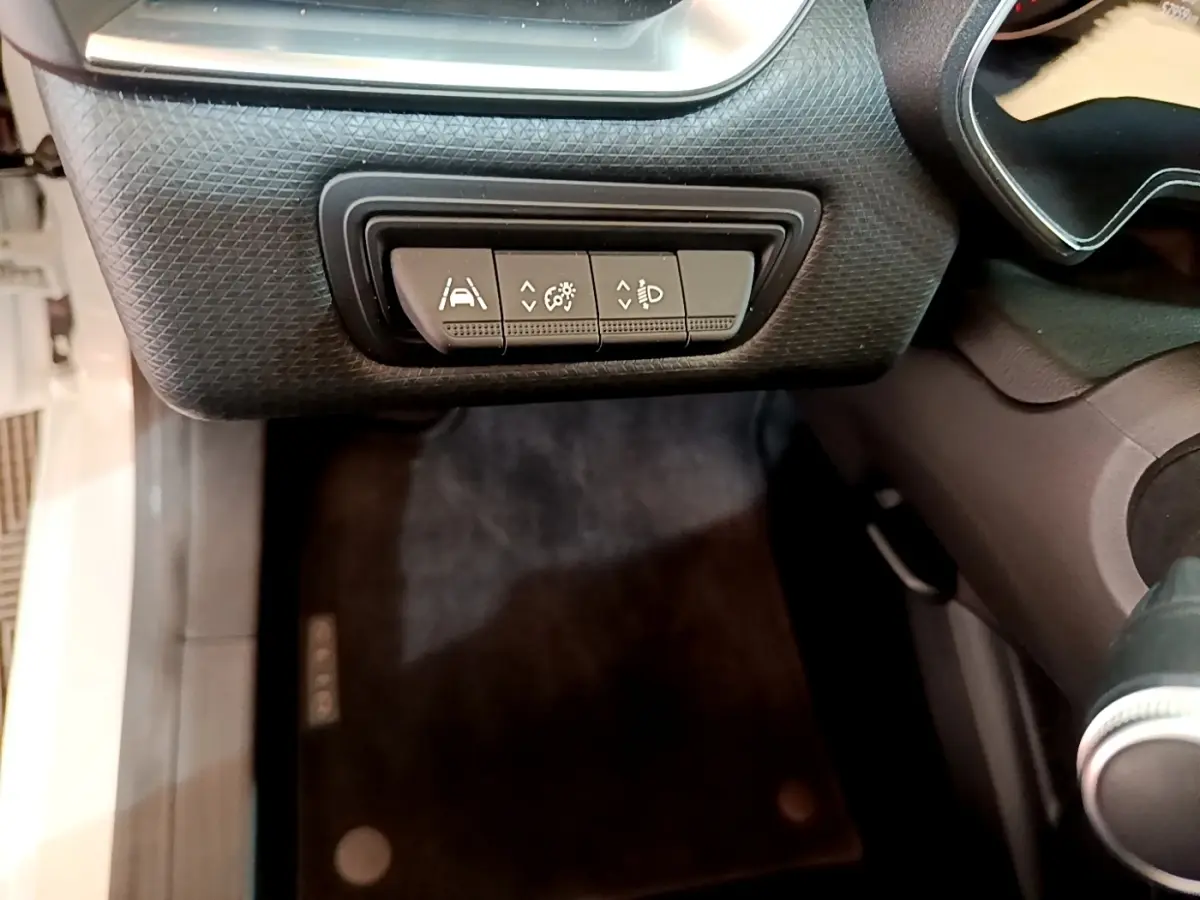 Gros plan sur les commandes de réglage d'assistance et éclairage côté gauche du tableau de bord d'une Renault Clio blanche.